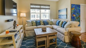 A living room with a sectional sofa, a coffee table, a TV, and artwork on the walls. - Brand New! 4-Br Bayside Townhome, Water and Pool View, Beach 1 block,  Free WiFi (Ocean City)