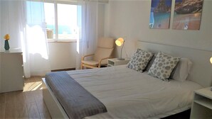 A bedroom with a bed, a chair, a bedside table, and a lamp. - MiraPraia 7- Refurbished, Air Conditioning, Wifi, TV, Bedroom and Living Room, Sea View (Quarteira)