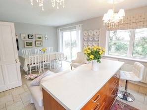 A bright kitchen with a central island, white cabinetry, and a dining area with chairs and a table. - Pretty Cottage in Louisburgh a perfect location to explore The Wild Atlantic Way (Louisburgh)