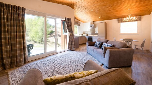 A cozy living room with a sofa, a rug, and a dining area with a table and chairs. - Deerstalker. Beautiful 5 star, 1 bedroom chalet sleeps up to 2 (Crianlarich)