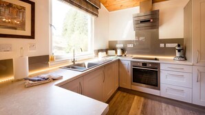 A modern kitchen with a wooden ceiling, stainless steel appliances, and a window with blinds. - Deerstalker. Beautiful 5 star, 1 bedroom chalet sleeps up to 2 (Crianlarich)