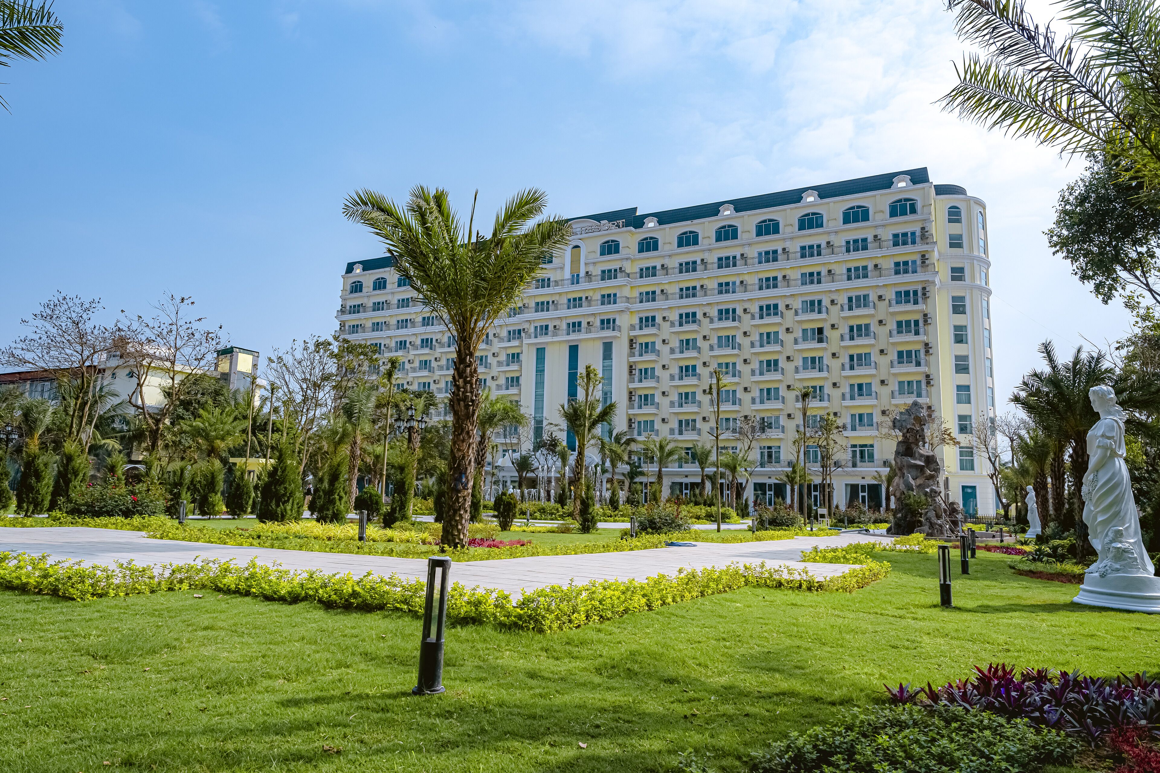 Un hotel grande con varios pisos, rodeado de jardines cuidados y palmeras.