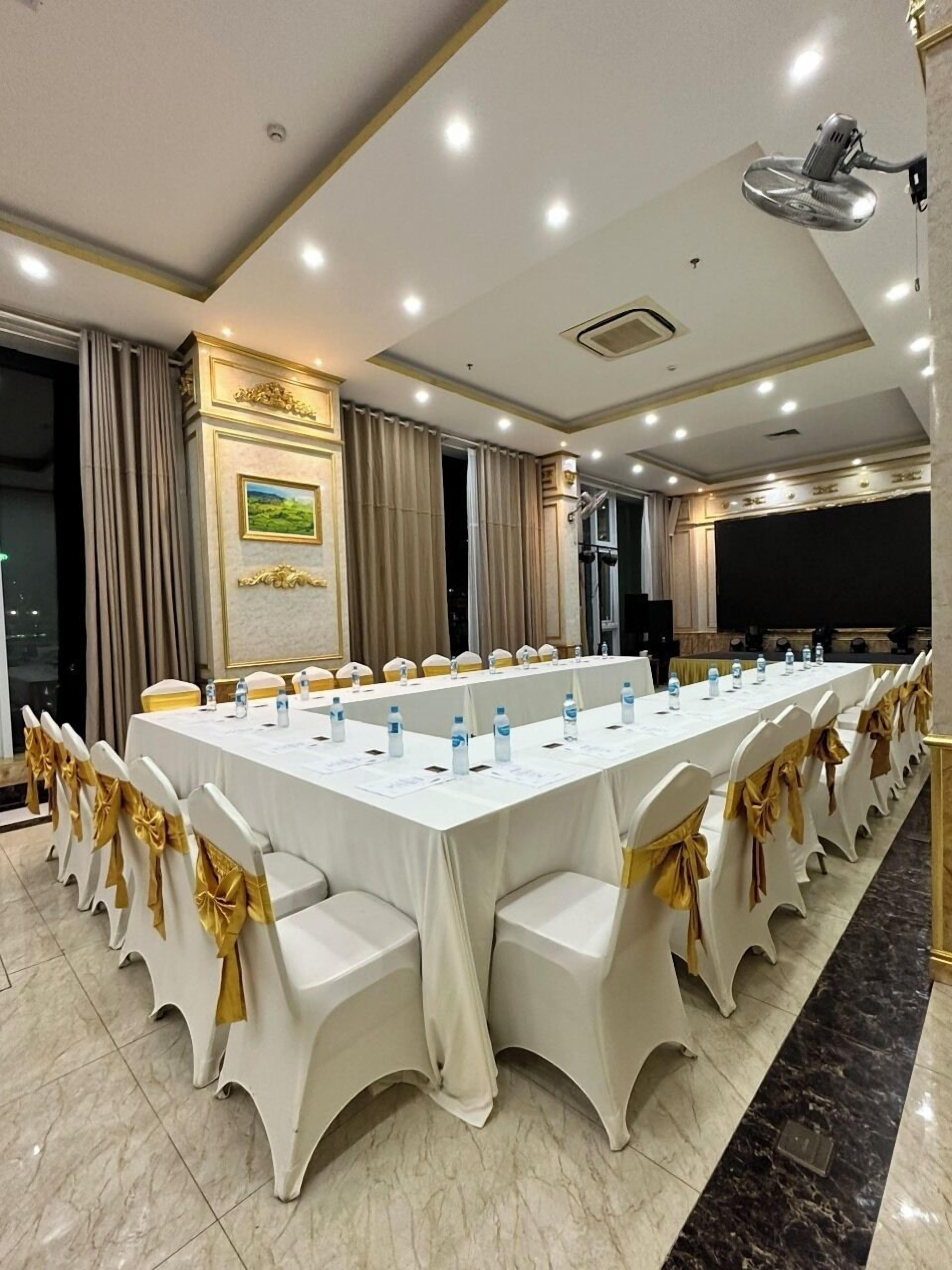 A conference room with a long table, white chairs with gold sashes, and a large screen.