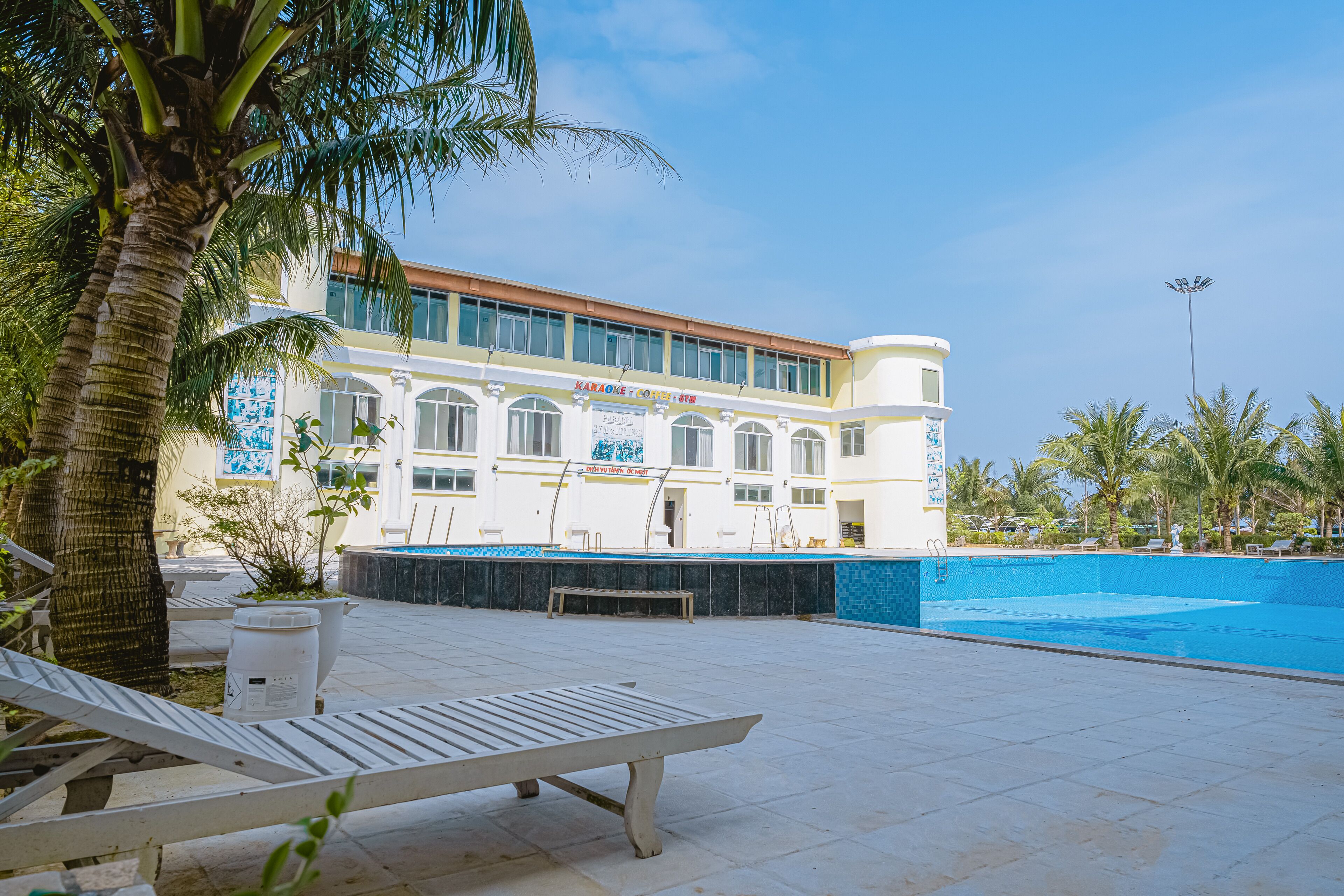 Un hotel con piscina, sillas de descanso y palmeras.