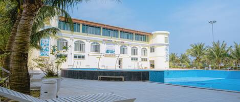 Un hotel con piscina, sillas de descanso y palmeras.