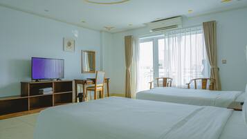 A hotel room with two beds, a desk with a chair, a television, and a large window with curtains.