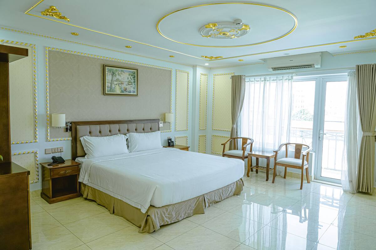 Ein geräumiges Hotelzimmer mit einem großen Bett, einem Schreibtisch, zwei Stühlen und einem großen Fenster mit Vorhängen.
