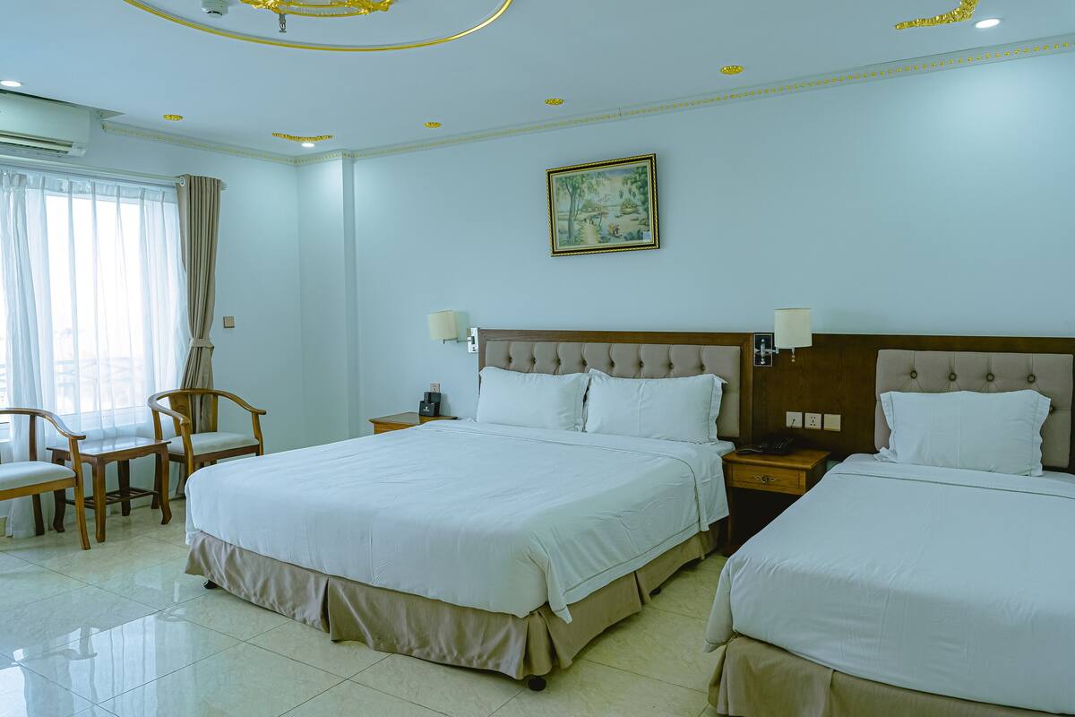 Ein Hotelzimmer mit zwei Betten, einer Sitzecke mit Sesseln, einem Gemälde an der Wand und einer Decke mit Einbautenleuchten.