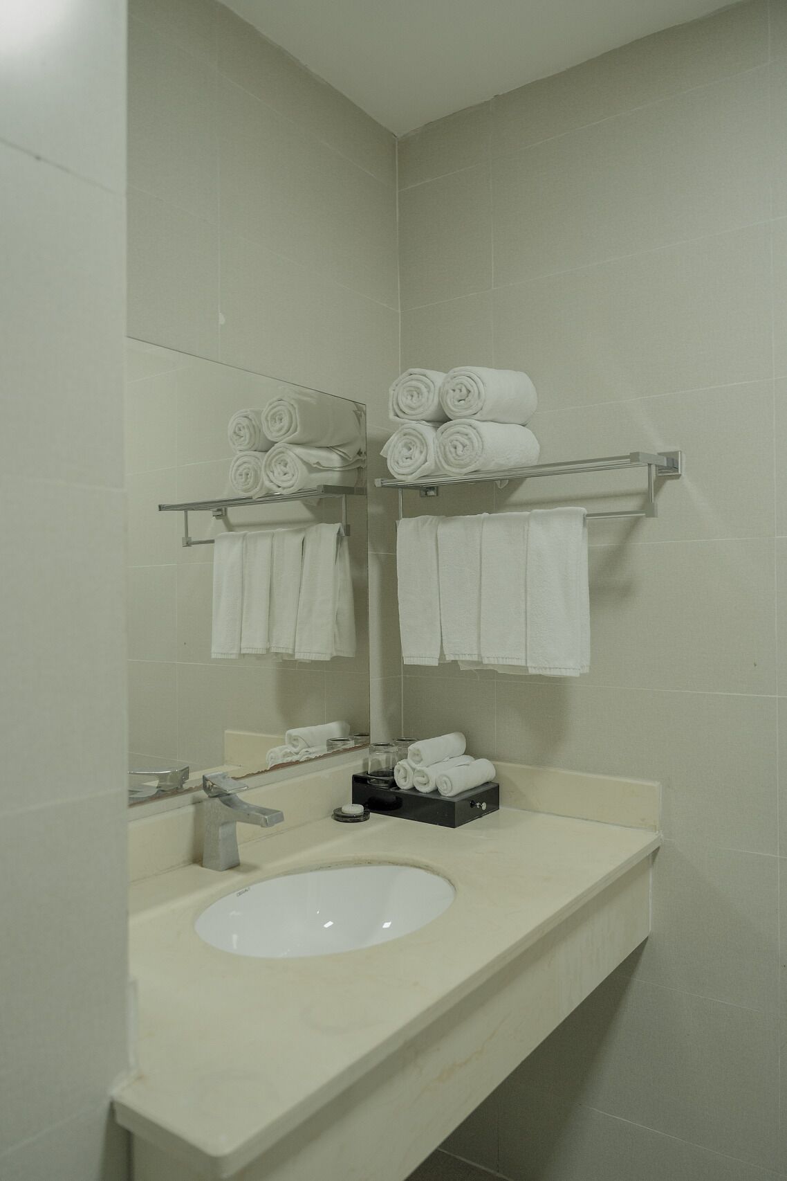 A bathroom with a sink, mirror, towel rack, and a tray with rolled towels.