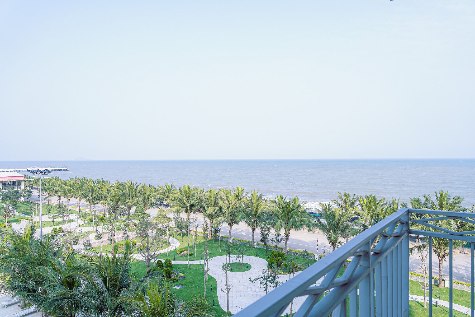 A coastal view with a promenade lined with palm trees and a pier in the distance.