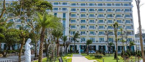 A multi-story hotel with a central courtyard, featuring a statue, benches, and well-maintained greenery.
