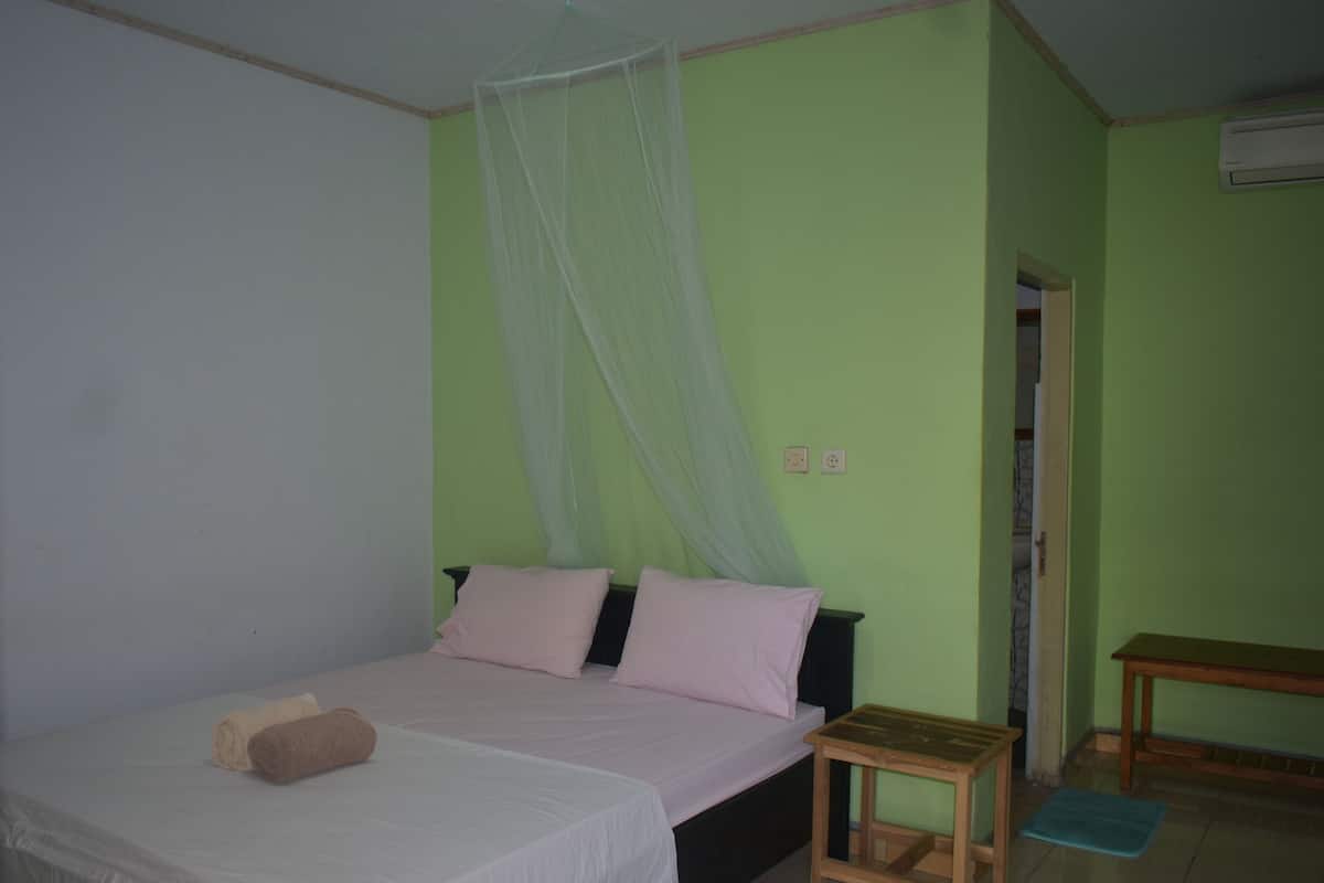 A bedroom with a bed, a bedside table, a bench, and a door leading to another room.