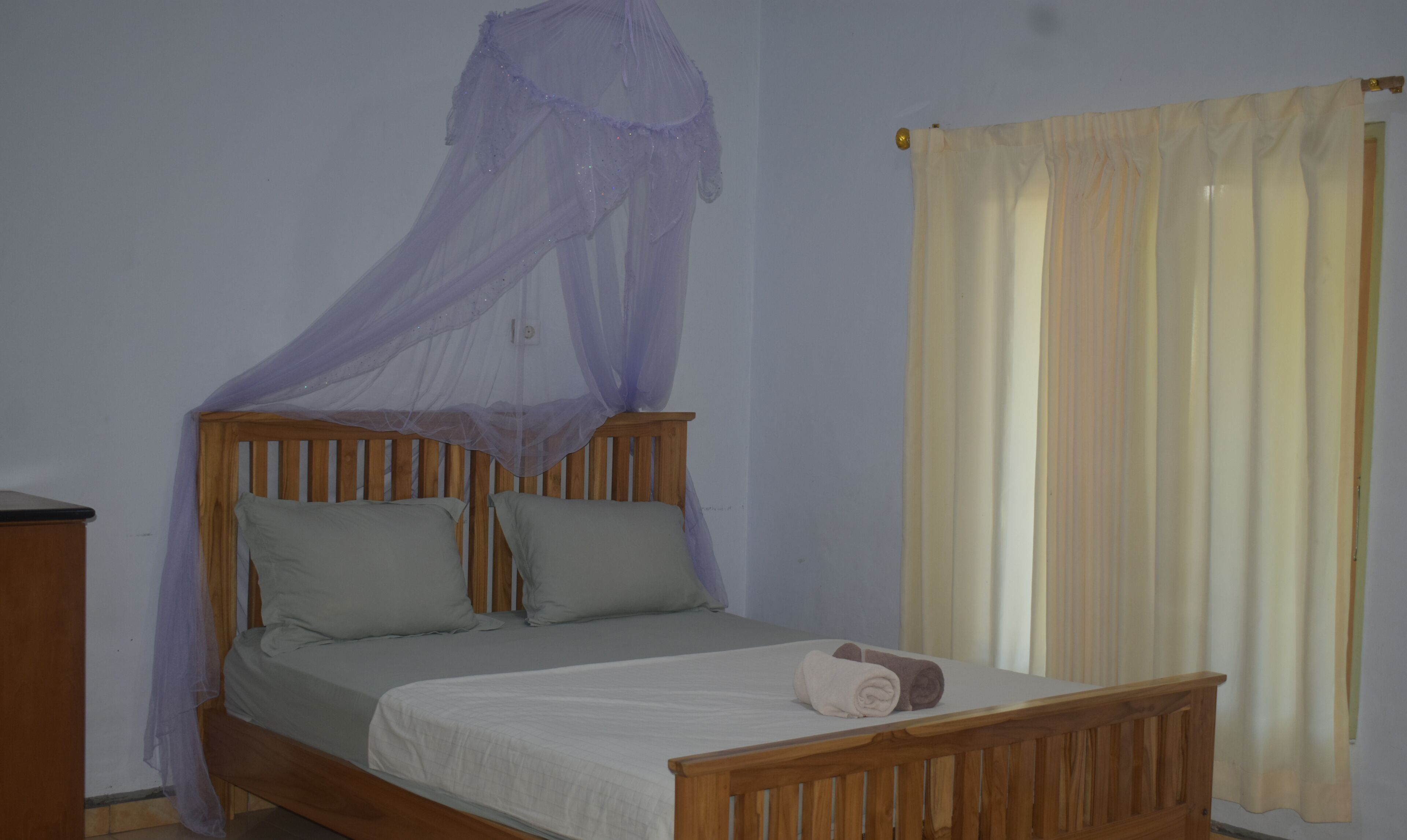 Una cama individual con estructura de madera, mosquitera y una toalla enrollada en el cabecero.