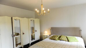A bedroom with a bed, a nightstand, a lamp, a chandelier, and a wardrobe with mirrors.