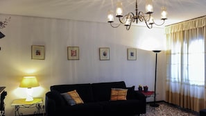 A living room with a black sofa, a table lamp, a floor lamp, and a chandelier. There are four framed pictures on the wall.