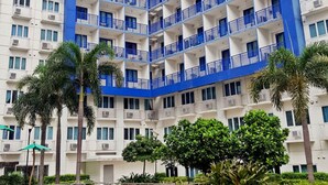 A high-rise hotel with multiple balconies, a swimming pool, and surrounding greenery. - Jericho's Place at Sea Residences (Pasay)