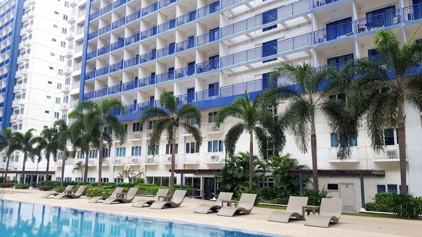 A high-rise hotel with multiple balconies, a swimming pool, and palm trees. - Jericho's Place at Sea Residences (Pasay)