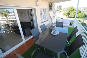 A balcony with a glass door leading to a room, a table with chairs, and a small garden area with artificial grass. - FAMILY DELUXE APARTMENT BEACH (CASTELLDELFELS)