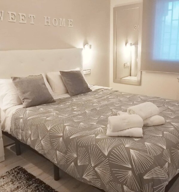 A neatly made bed with a patterned bedspread, two pillows, and a set of towels on the side.
