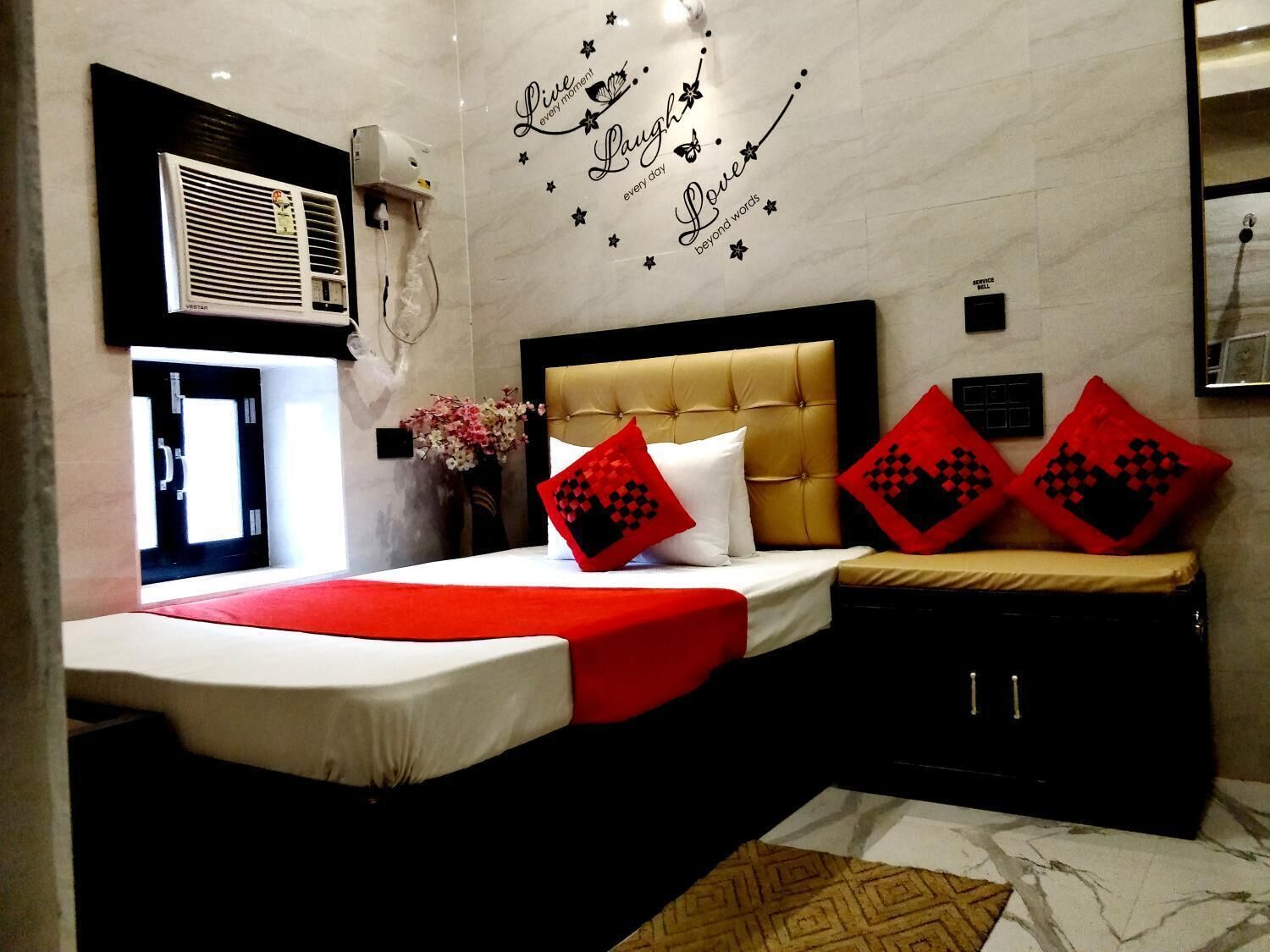 Une chambre d’hôtel comprenant un lit, un climatiseur fixé au mur, un motif décoratif sur le mur et un petit meuble de rangement.