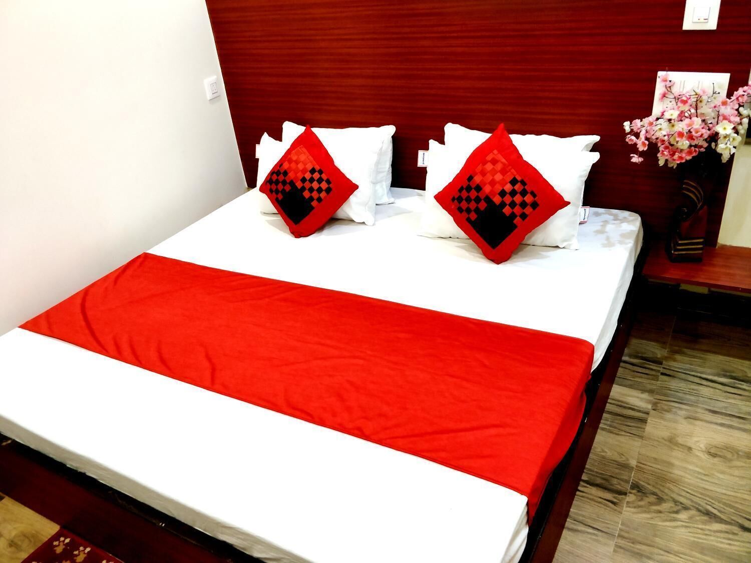 Une chambre d’hôtel avec un lit, une literie rouge et blanche, et une tête de lit en bois.