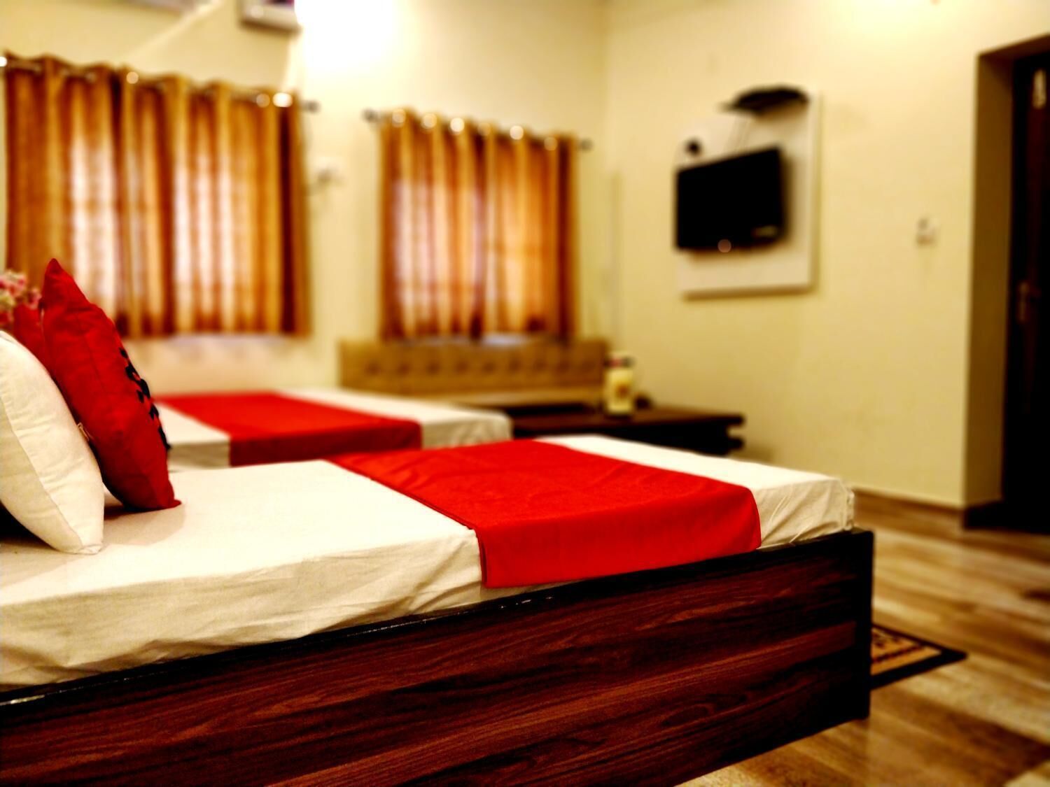 Ein Hotelzimmer mit zwei Betten, jeweils mit roter Decke und weißen Laken. Ein Fernseher ist an der Wand montiert und der Boden ist aus Holz.