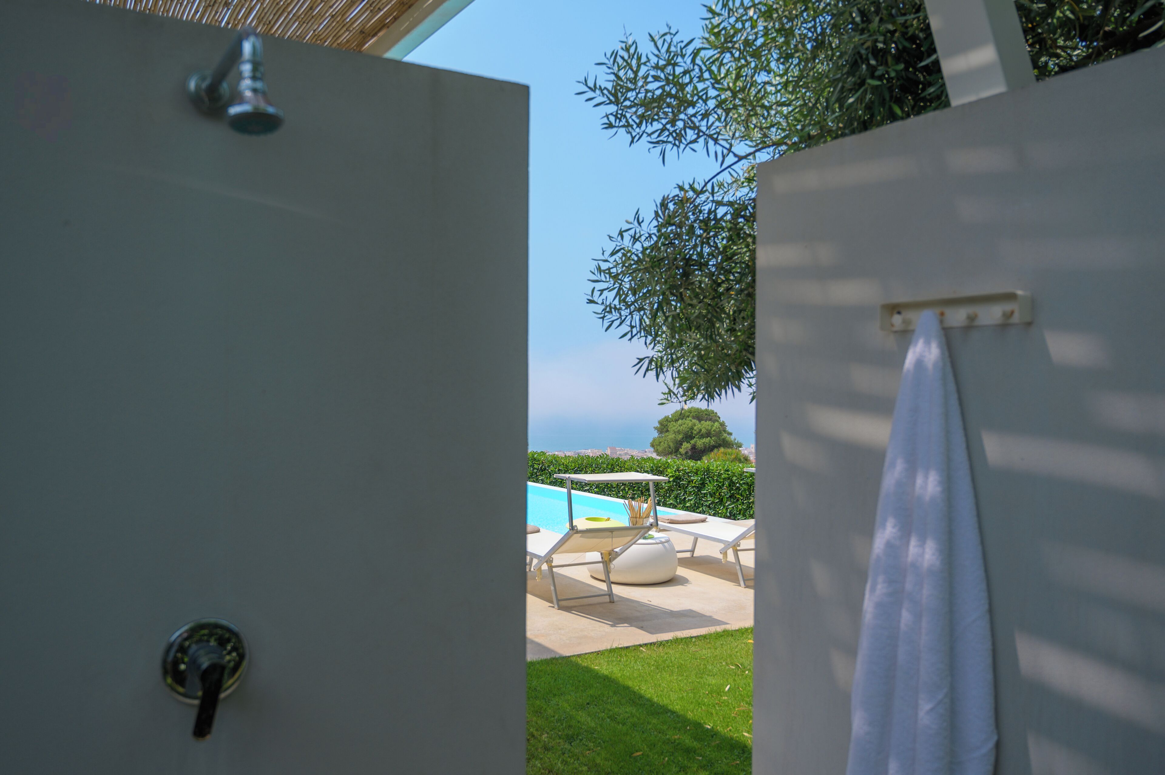Un baño con ducha, una toalla colgada en la pared y vistas a una piscina y zona de estar al aire libre.