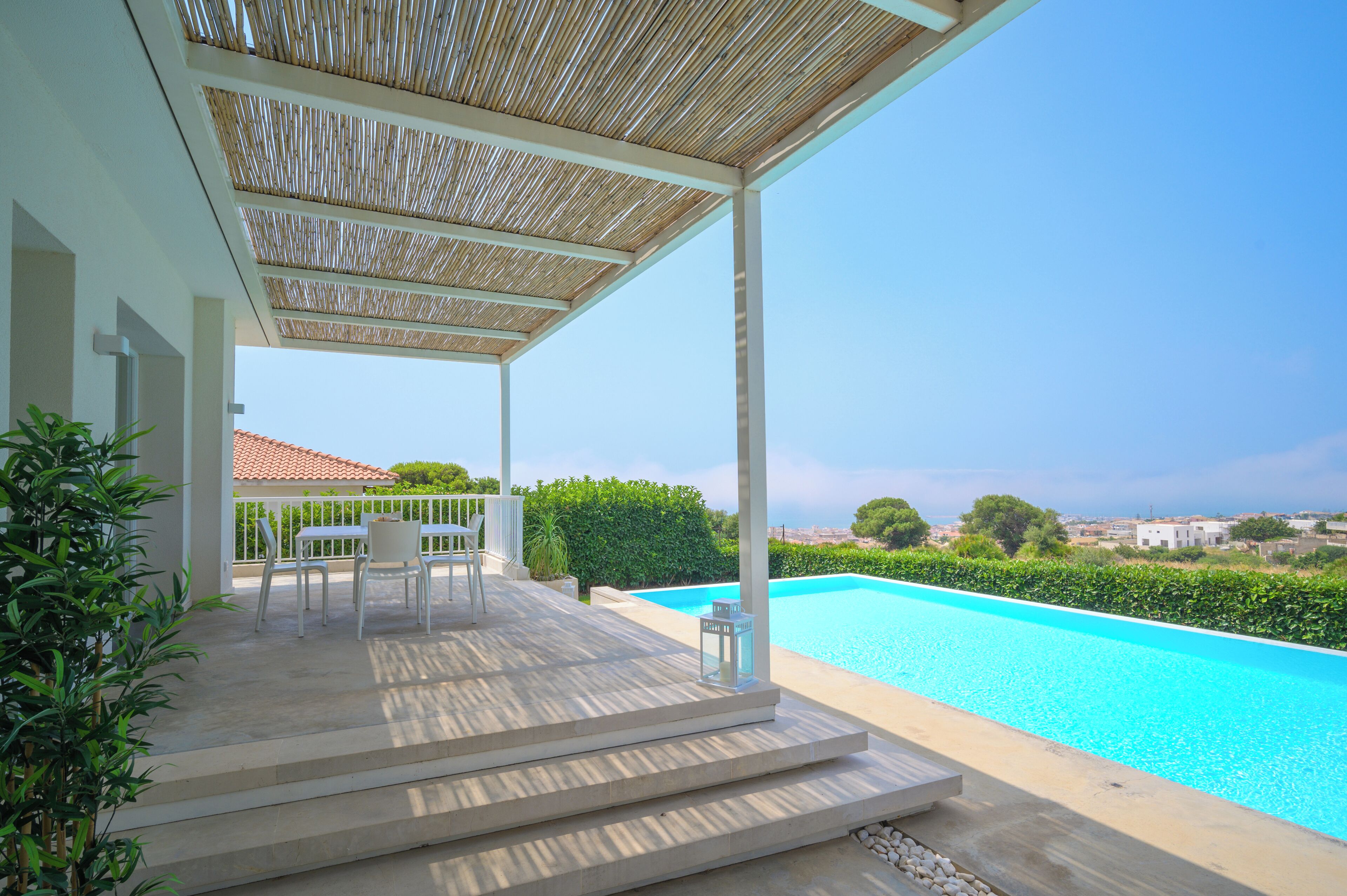 A covered outdoor area with a pool, steps leading to a terrace, and a view of the sea.