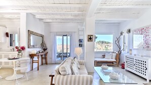 Een ruime woonkamer met een gestreept sofa, een glazen bijzettafeltje en uitzicht op het omliggende landschap.