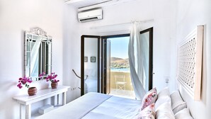 Een slaapkamer met een bed, een nachtkastje met een bloevas, een raam met uitzicht op het omliggende landschap, en een airconditioning.