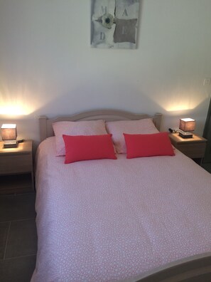 Ein Bett mit einem gemusterten Überwurf, zwei rote Kissen und zwei Nachttischlampen auf Holz-Nachttischen.