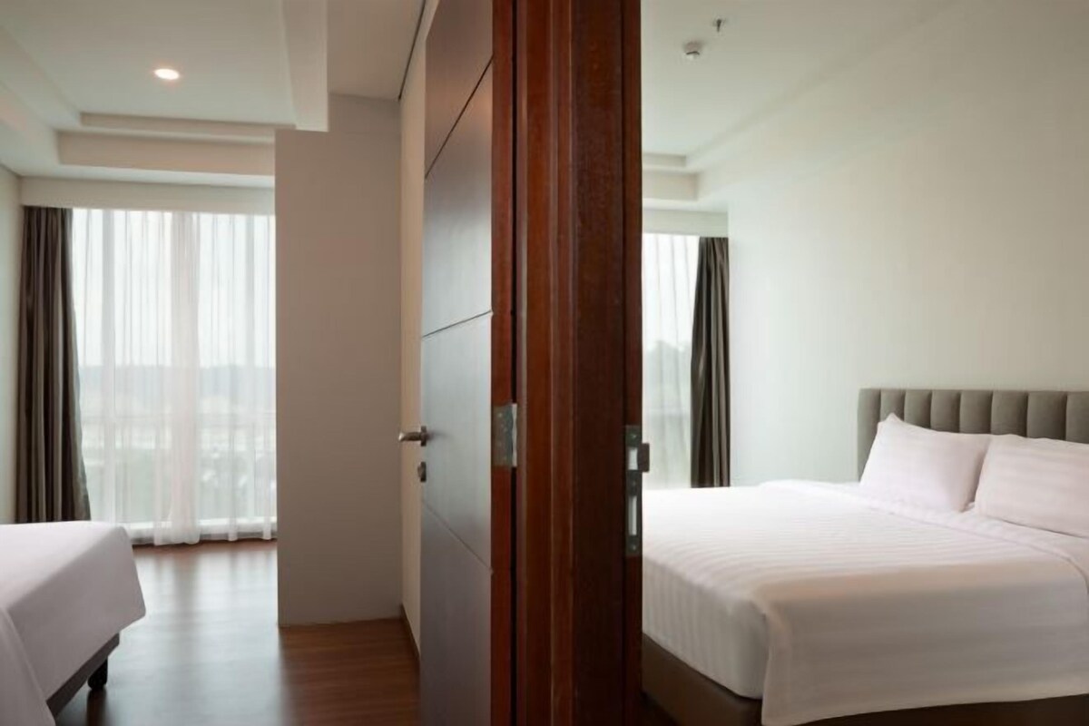 Una habitación de hotel con una cama, un armario de madera y vistas a la ciudad a través de amplias ventanas.