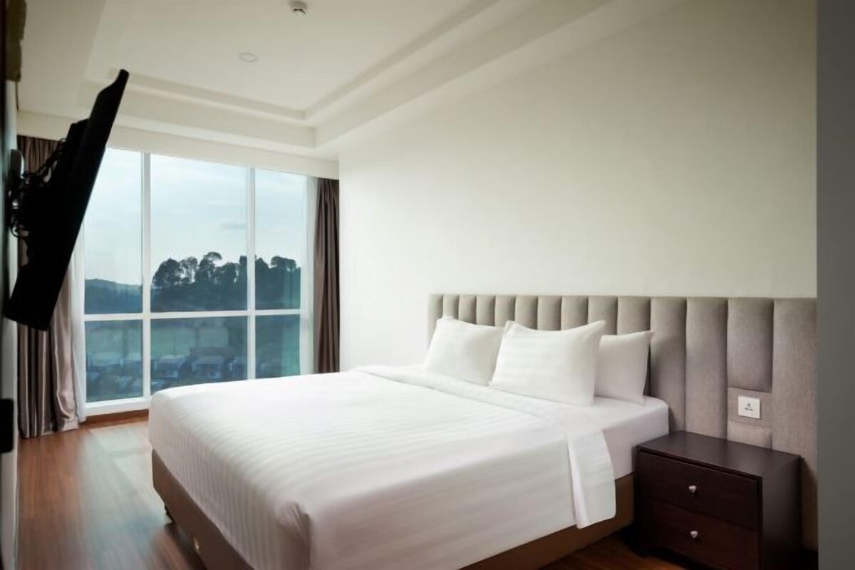 Habitación de hotel moderna con una cama grande, una mesita de noche y vistas a la ciudad a través de amplios ventanales.