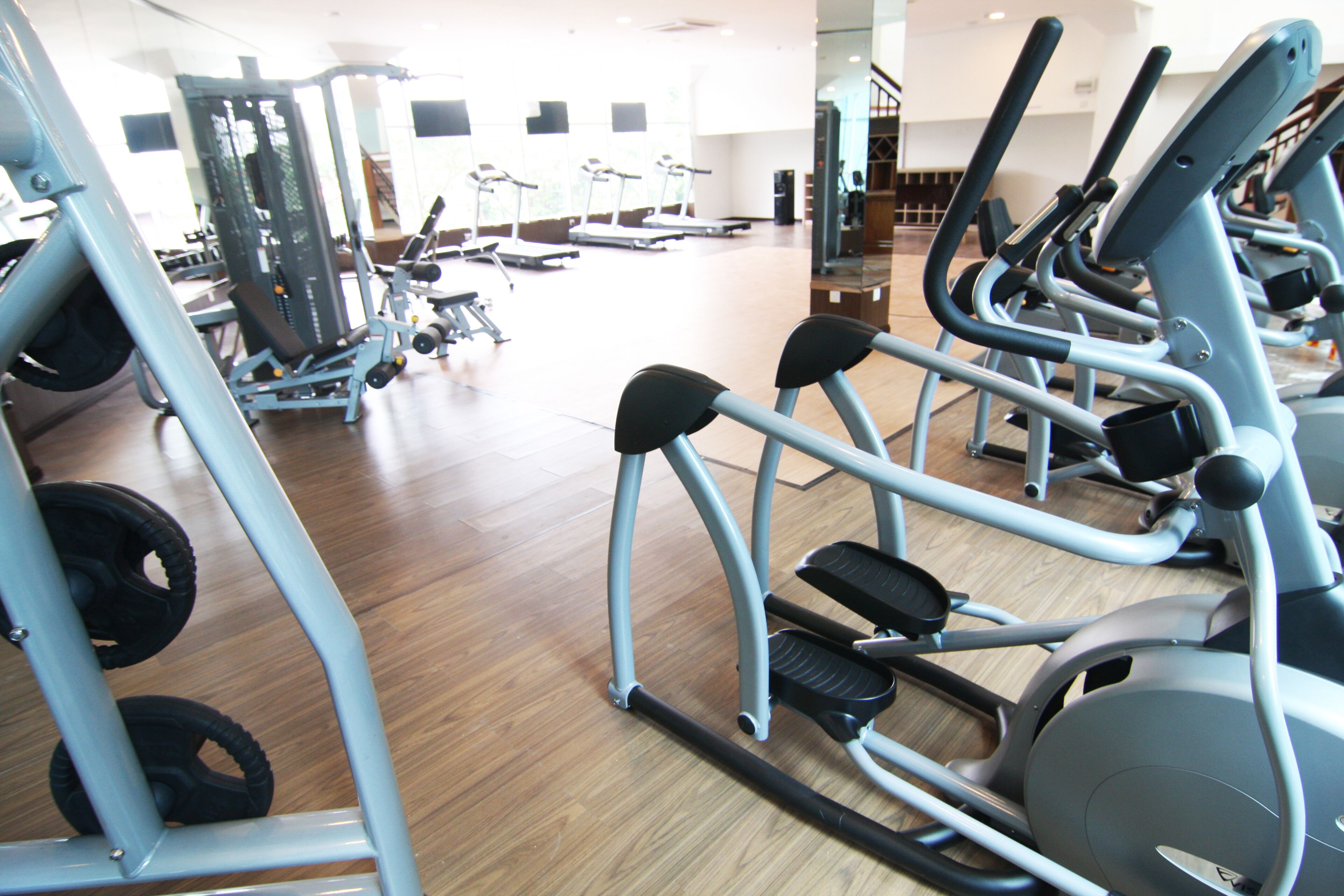 A gym with various exercise machines, including treadmills and elliptical trainers, arranged in rows.