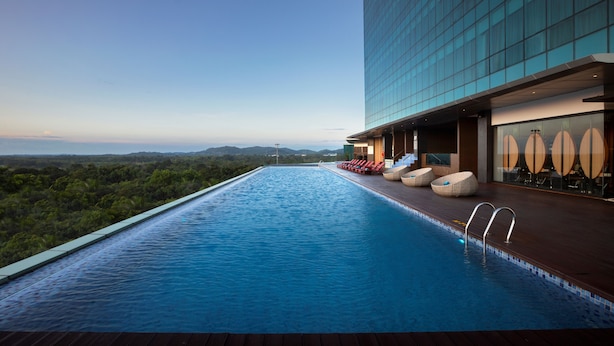 Una piscina infinita en la azotea con vistas a las montañas, sillas de descanso y un edificio de cristal.