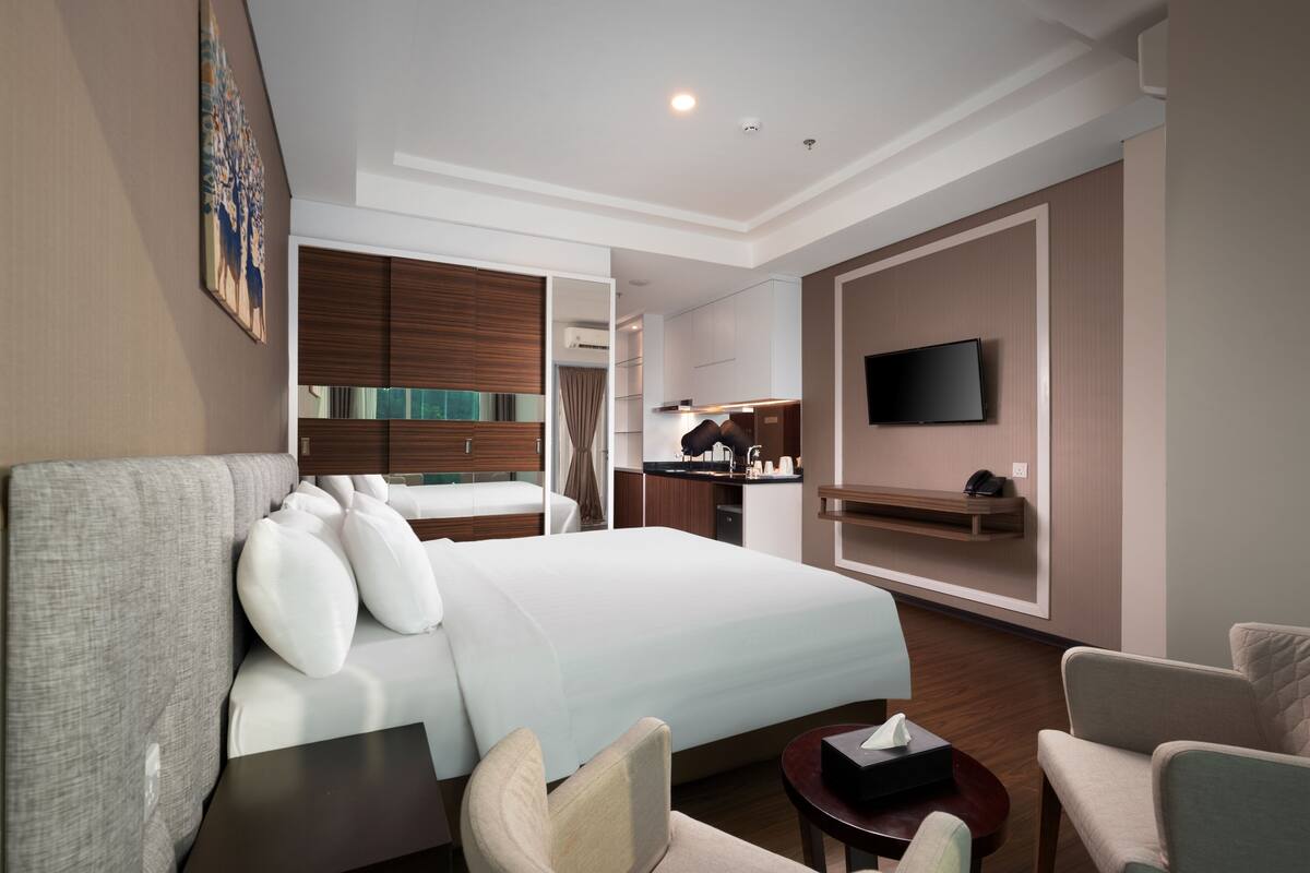 Una habitación de hotel con una cama grande, un escritorio, una silla, un televisor y una kitchenette.