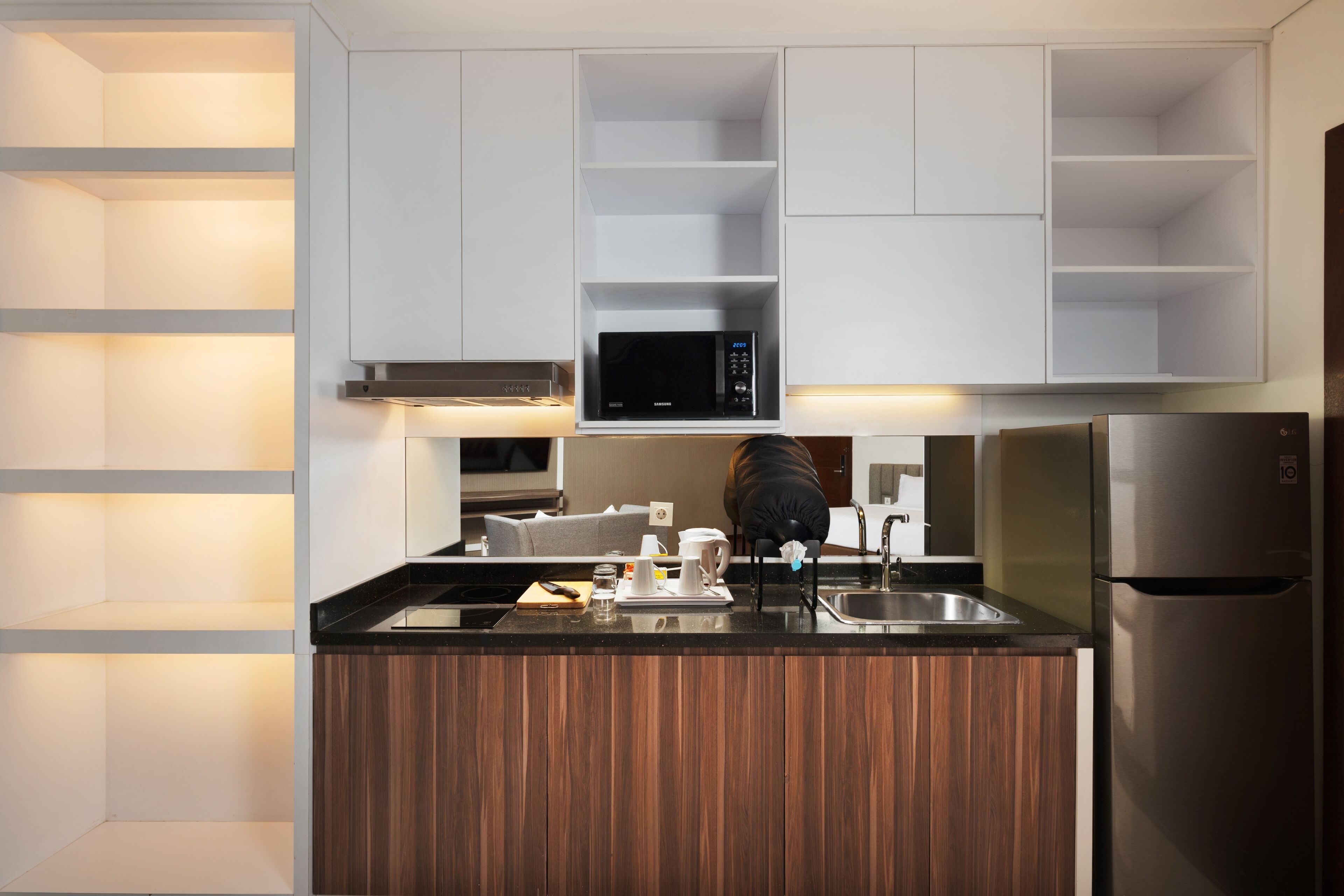 A modern kitchen with white cabinets, a built-in microwave, a stainless steel refrigerator, and a wooden island with a sink.