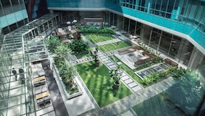 Un edificio moderno con fachada de vidrio, un patio central con zonas de estar y un pequeño jardín.