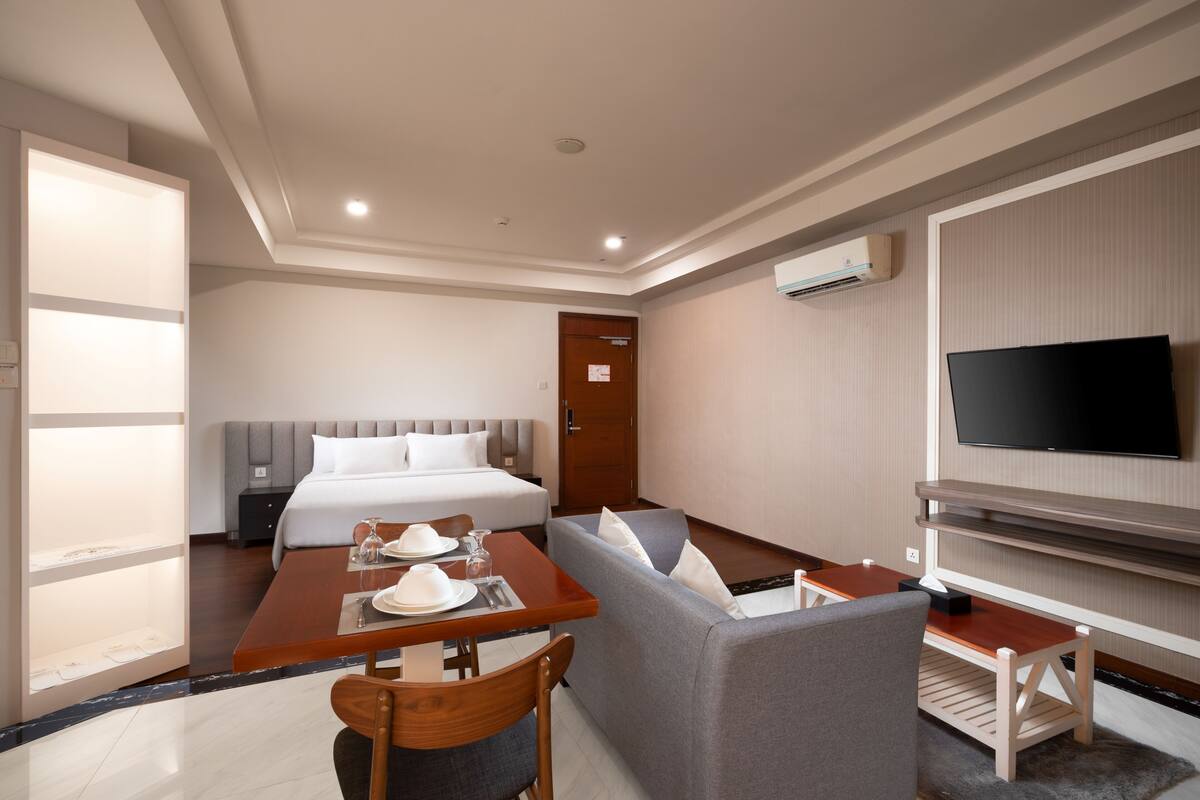 Una habitación de hotel con cama, televisor, mesa de comedor con sillas y sofá.