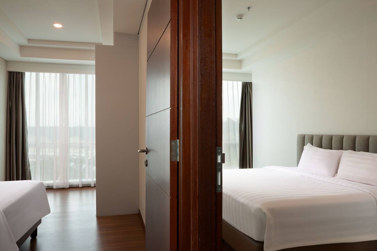Una habitación de hotel con una cama grande, un armario de madera y vistas a la ciudad a través de cortinas traslúcidas.