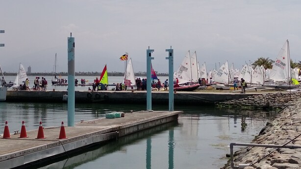 A marina with multiple sailboats docked, a pier with people, and a calm water body. - Da Peng Bay homestay (Linbian)