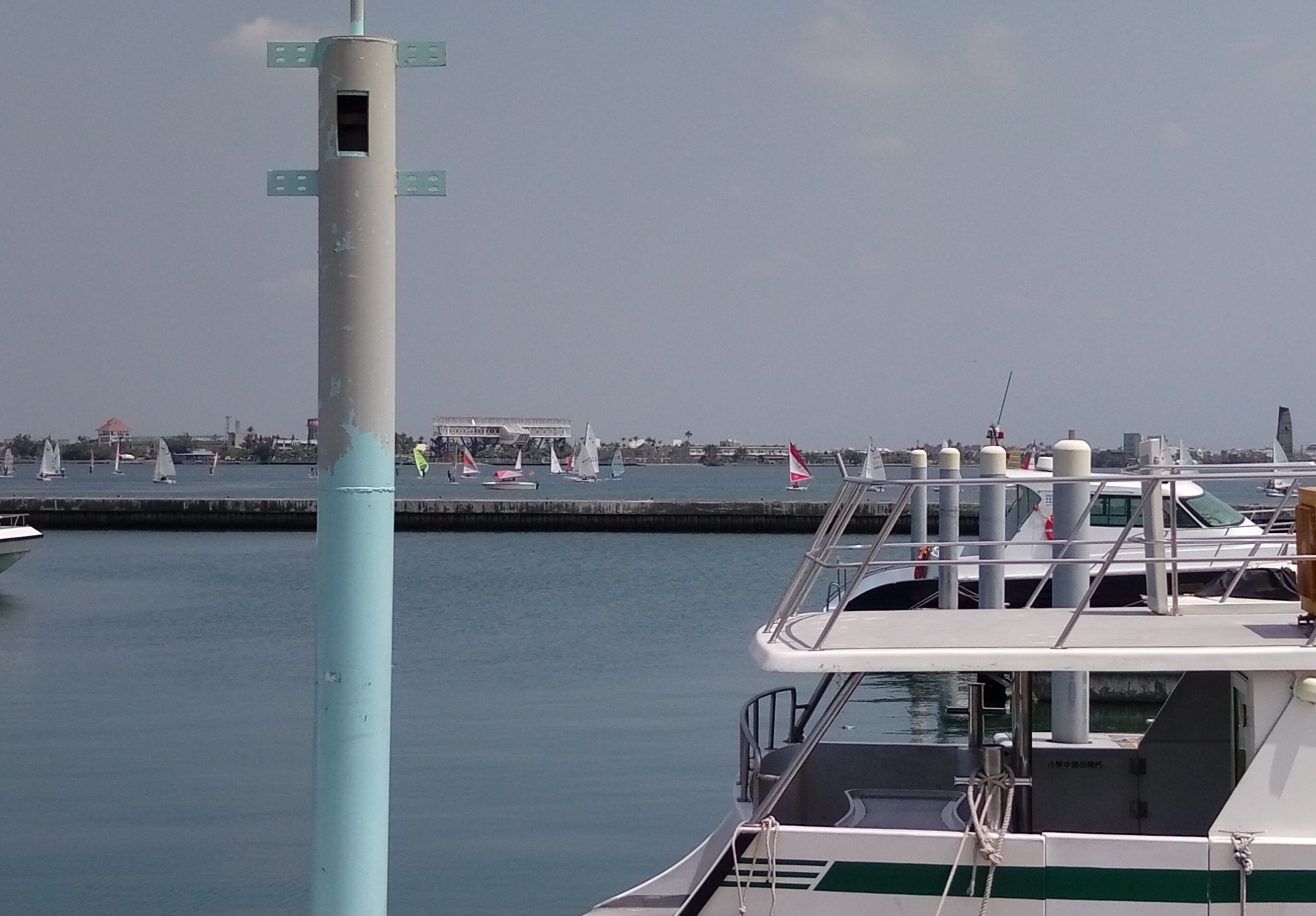 A marina with boats docked, a tall structure with directional signs, and a distant cityscape.