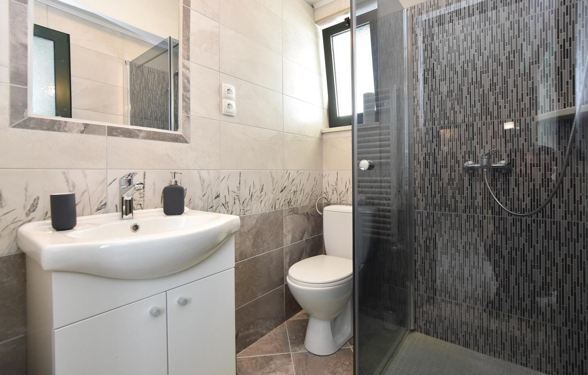 Un baño moderno con un lavamanos blanco, un inodoro y una zona de ducha con mampara de vidrio.