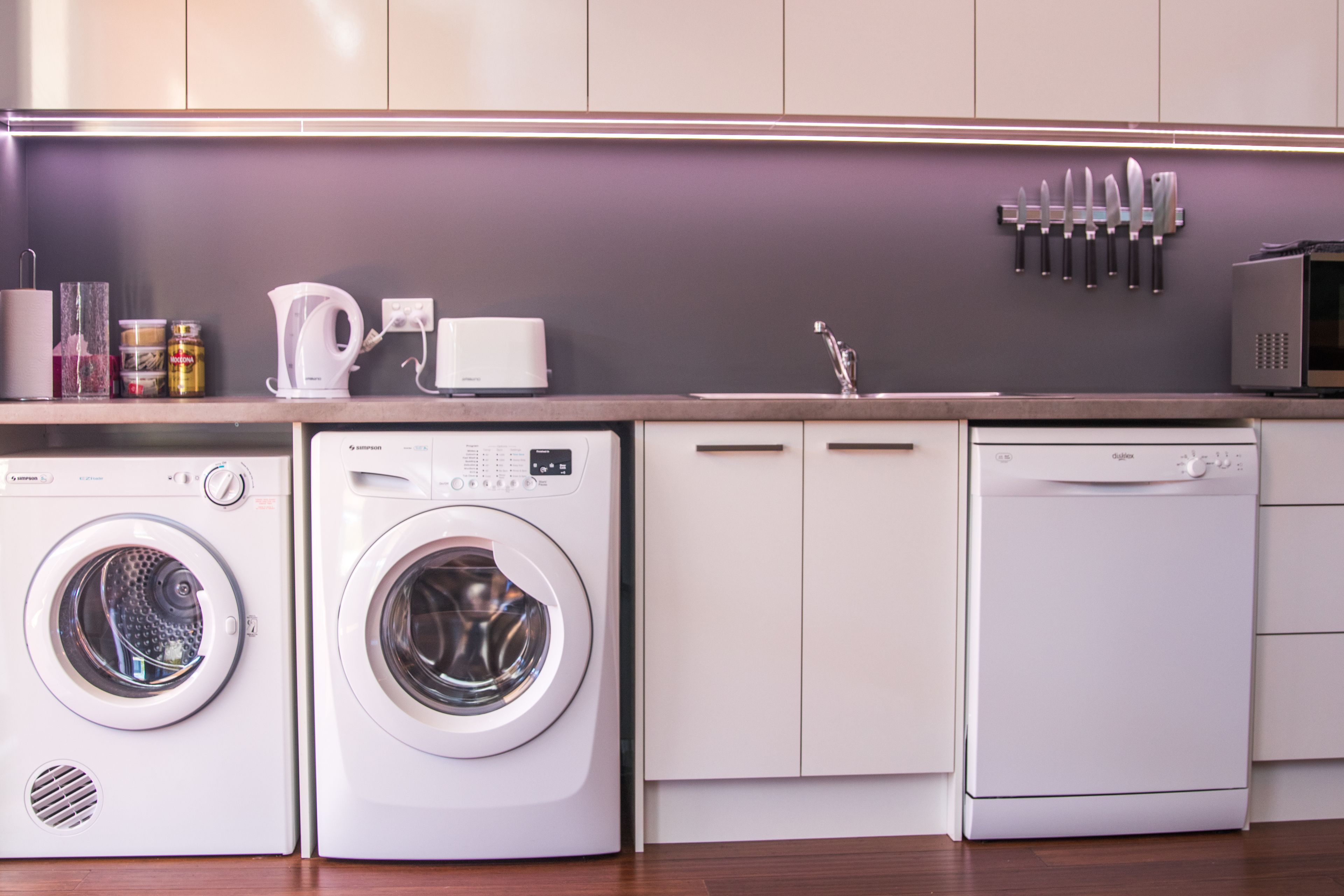 Une cuisine moderne équipée d’appareils électroménagers intégrés, notamment un lave-linge, un lave-vaisselle et un four à micro-ondes.