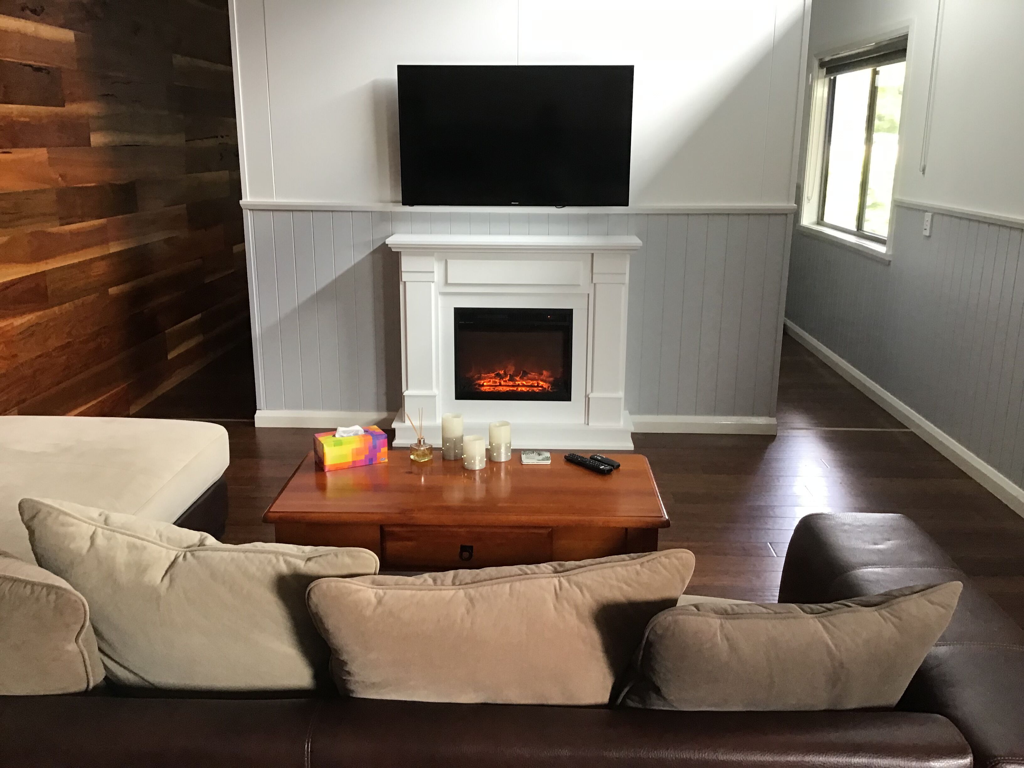 A living room with a fireplace, a television mounted above it, and a leather sofa with cushions.