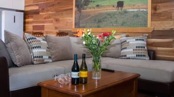 Un salón con pared de madera, un sofá con cojines estampados, una mesa de centro con botellas de vino y un florero con flores.