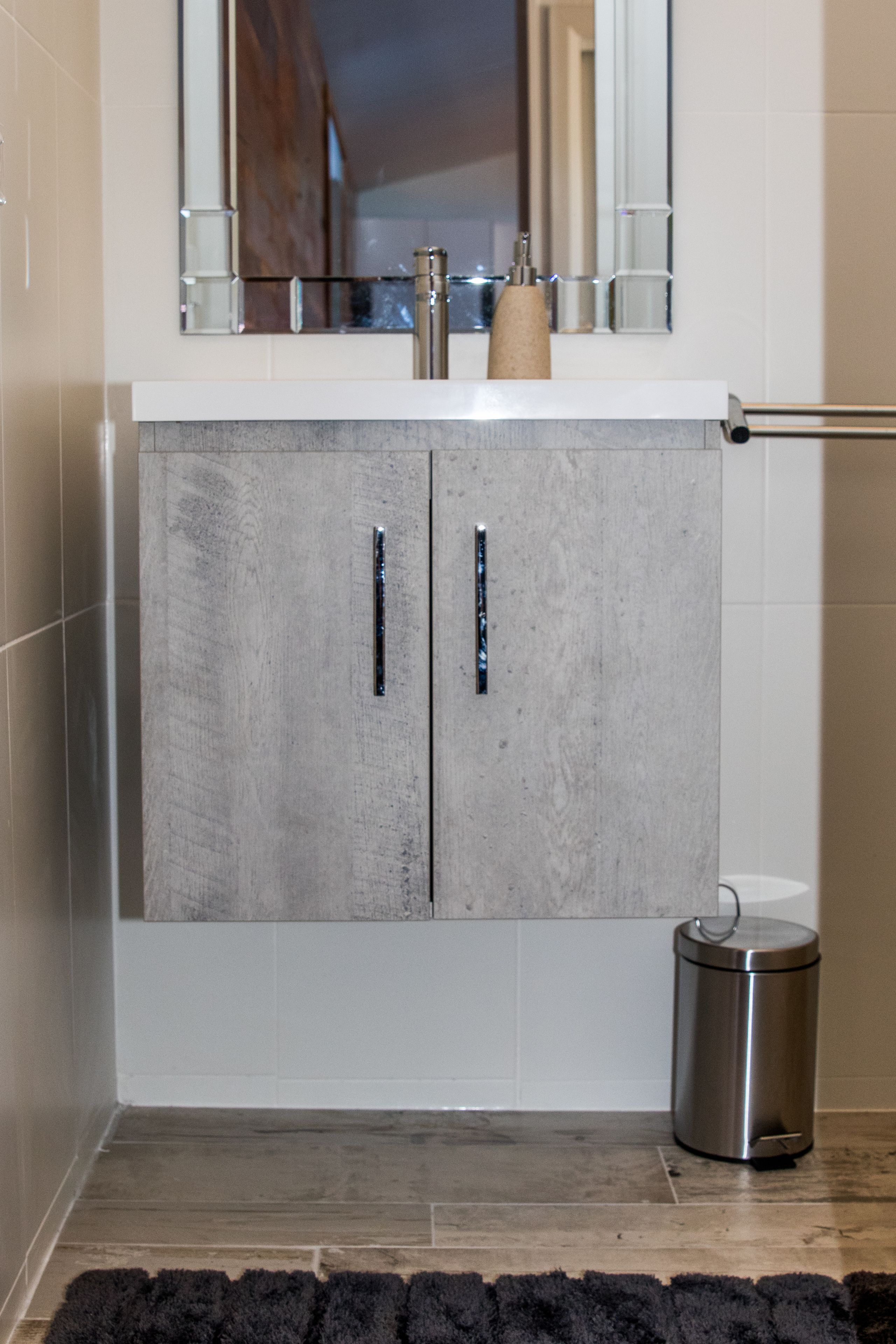 Un baño con un armario gris, un espejo y un cubo de basura.