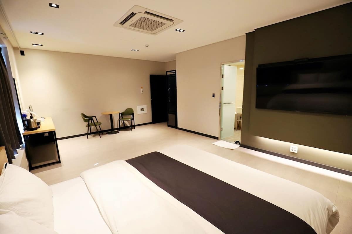 Une chambre d’hôtel comprenant un lit, un bureau avec une bouilloire, deux chaises, une télévision et une porte donnant sur une salle de bain.