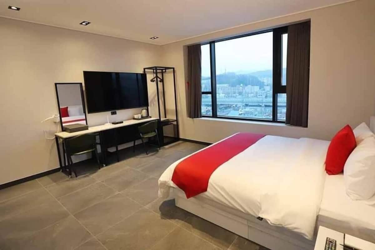 Une chambre d’hôtel équipée d’un lit, d’un bureau, d’une chaise, d’une télévision et d’une fenêtre donnant sur la ville.