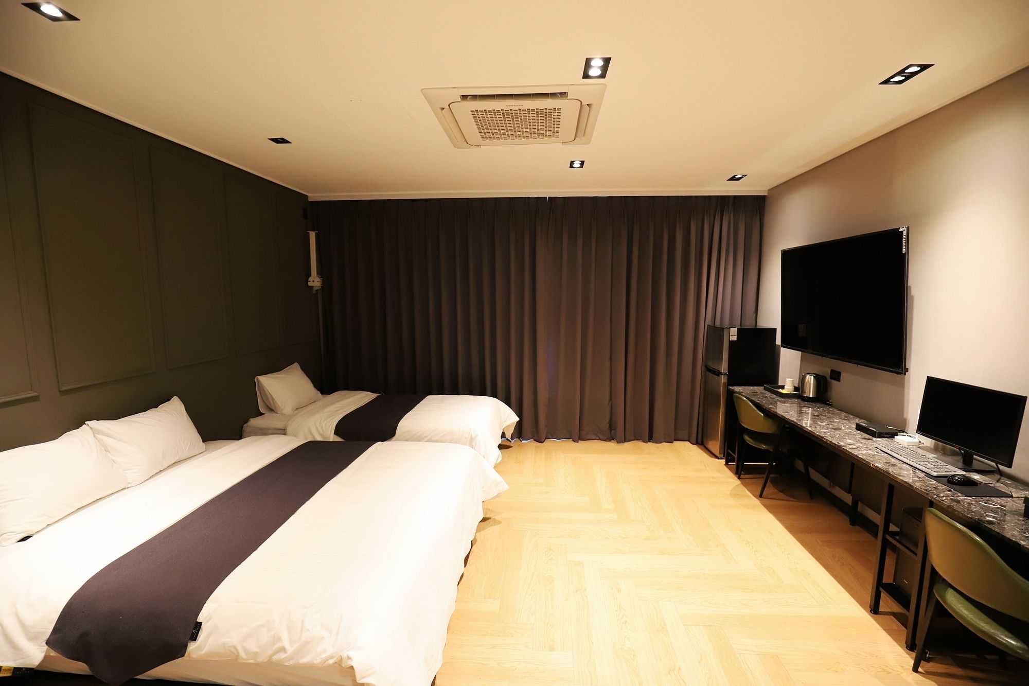 Habitación de hotel con dos camas, un escritorio con computadora, un televisor de pantalla plana y un refrigerador.